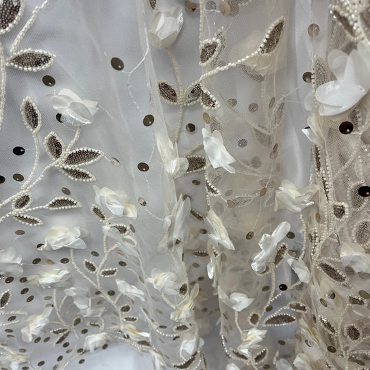 Close-up of a sheer white tulle fabric with embroidered floral and leaf patterns in white, pearl-bead, and metallic Champagne tones.