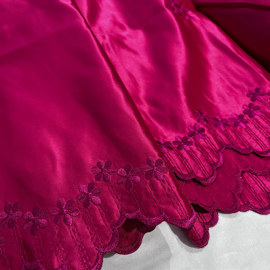 A close-up of a fuchsia satin fabric with a scalloped embroidered border featuring floral details.