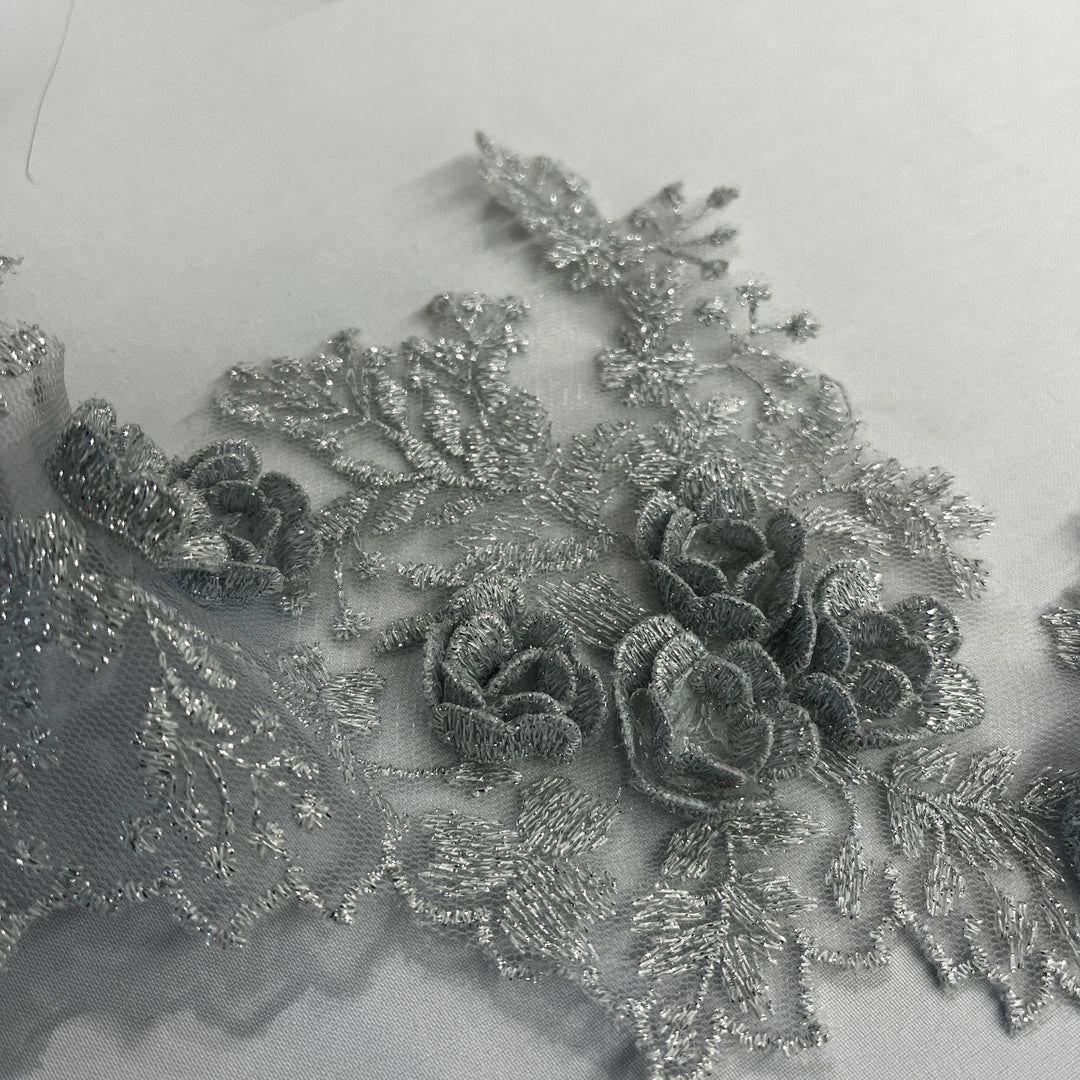  Closeup of Silver lace trim with 3D rose motifs embroidered with metalic thread on 100% polyester net mesh, on a white background. LaceUSA #21853W
