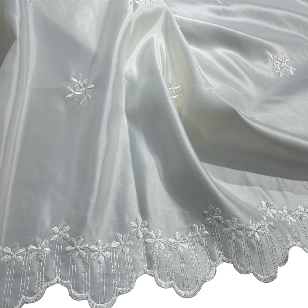 Ivory satin fabric with a scalloped embroidered border and small floral embroidery details, draped to show its texture and sheen.