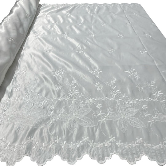 Ivory embroidered satin fabric with a scalloped lace border and floral vine patterns, shown partially rolled on the left.