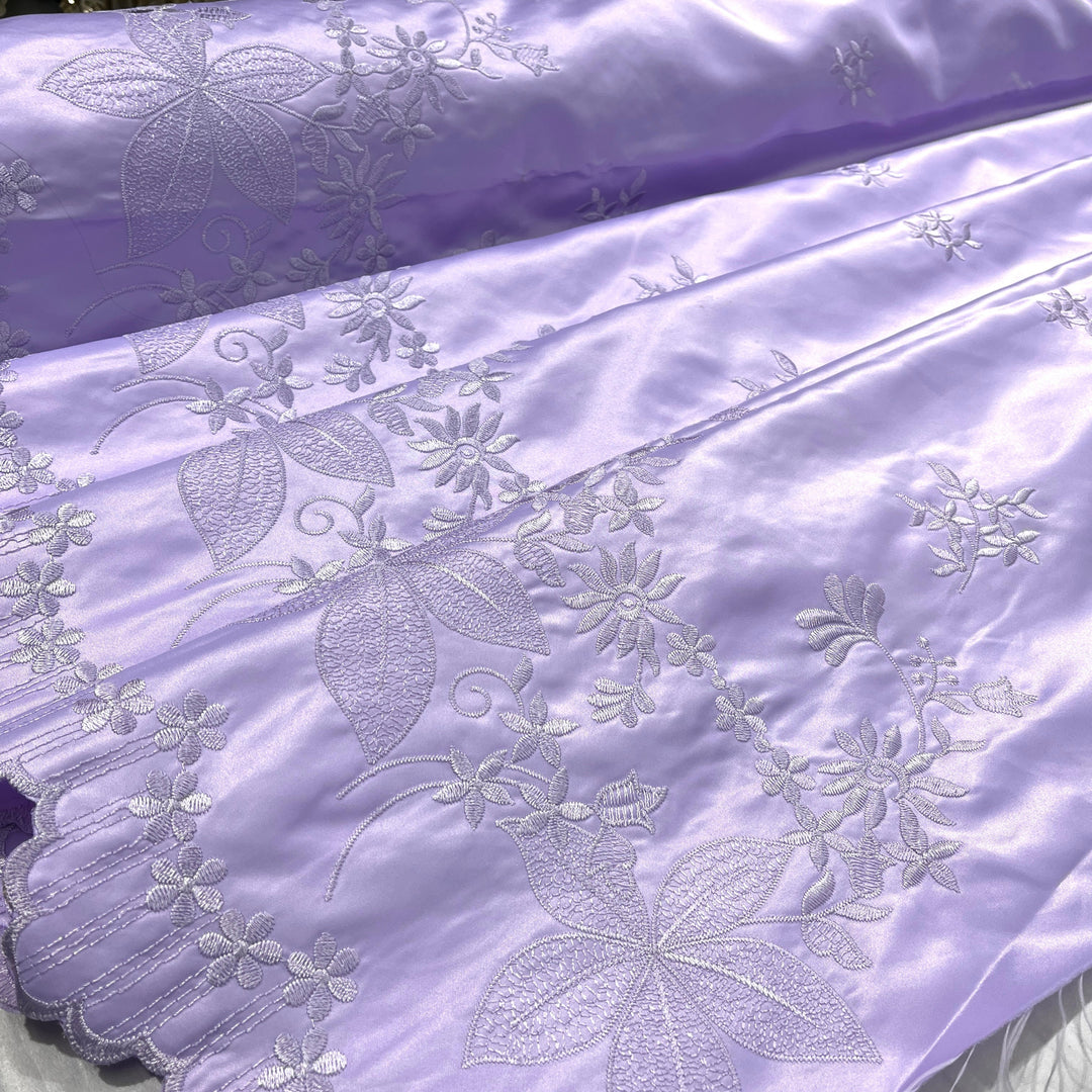 Lilac satin fabric with floral and leaf embroidery, featuring a scalloped edge.