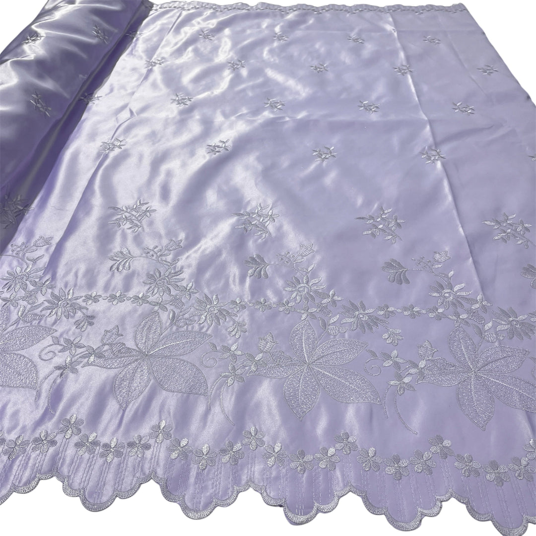 Lilac embroidered fabric with floral and leaf patterns, featuring a scalloped edge and a matching rolled section on the left.