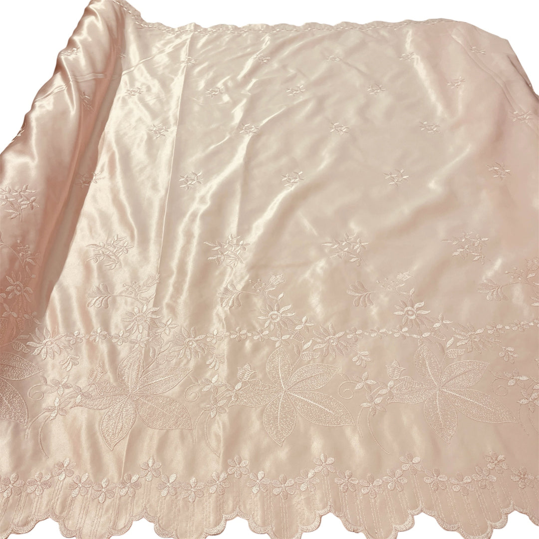 A light peach satin fabric with delicate floral embroidery and a scalloped embroidered border, shown laid flat against a white background.