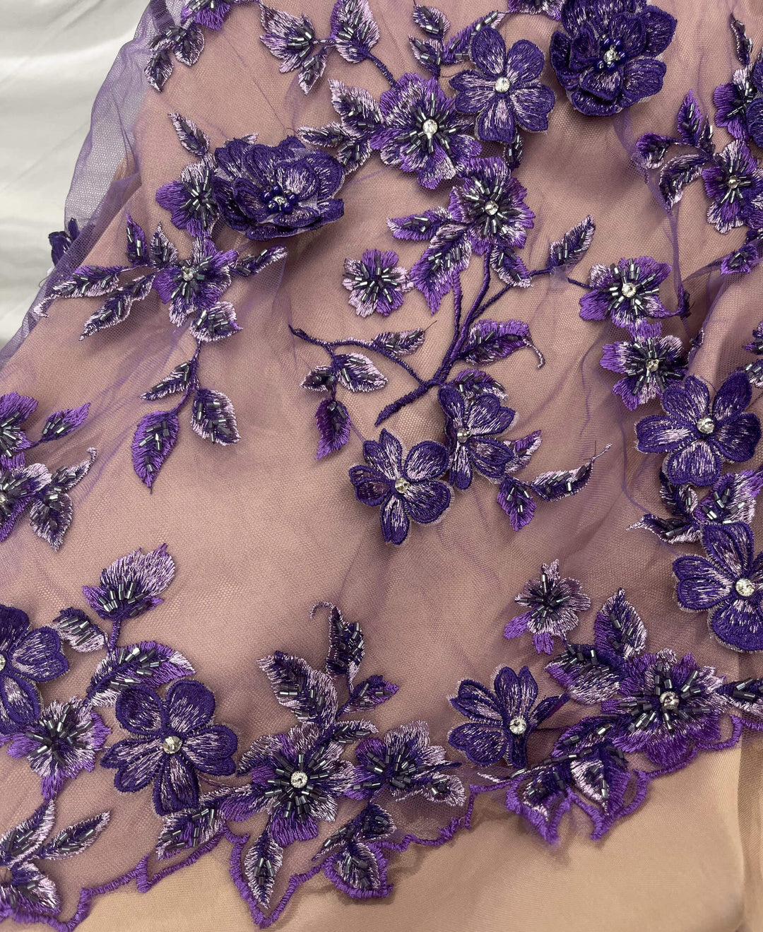 Closeup 
 of Purple Beaded 3D Floral Lace  embroidered on Net Mesh displayed on champagne fabric- LaceUSA GD1613