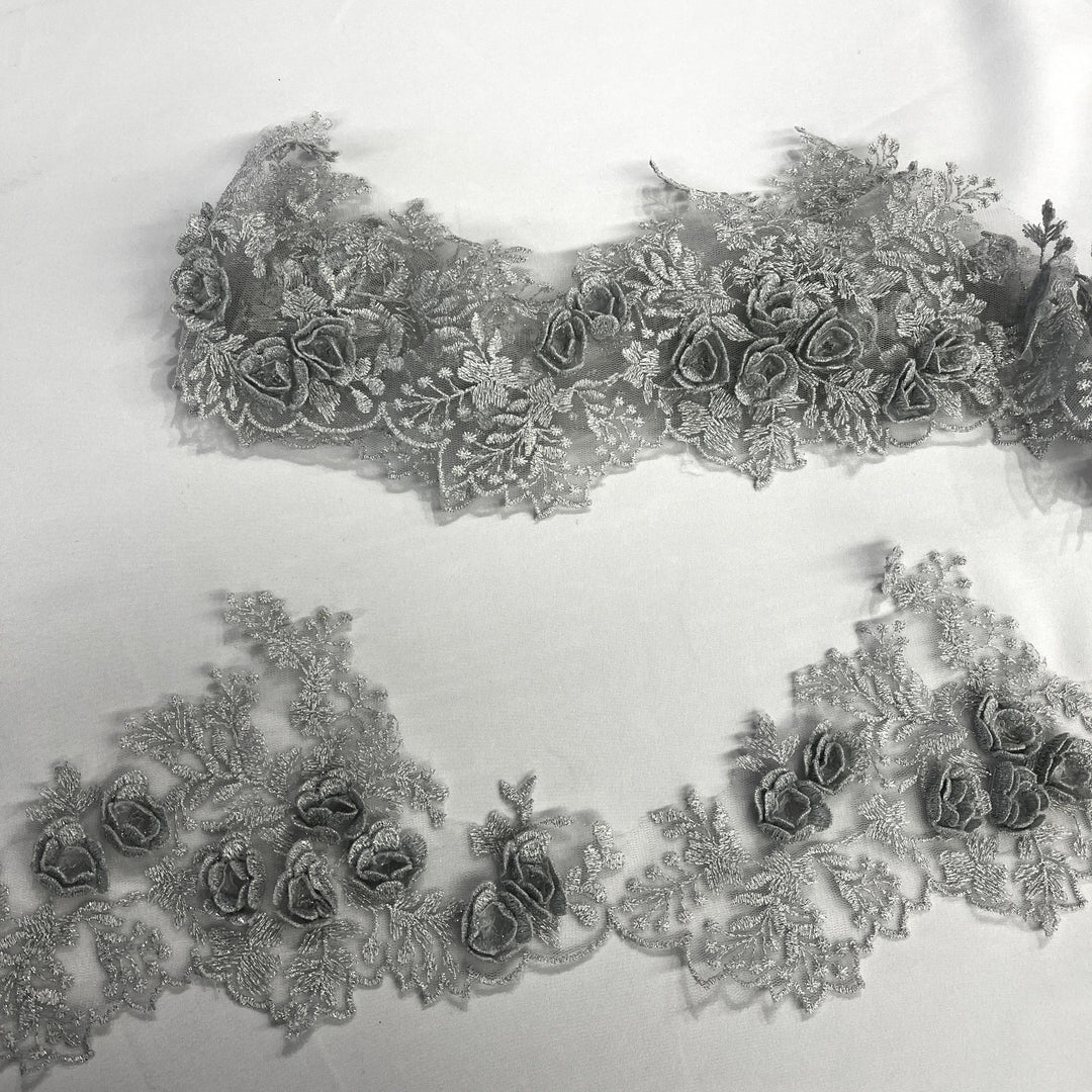 Silver lace trim with 3D rose motifs embroidered with metalic thread on 100% polyester net mesh, featuring one flat unrolled length and one gathered bundle on a white background. LaceUSA #21853W