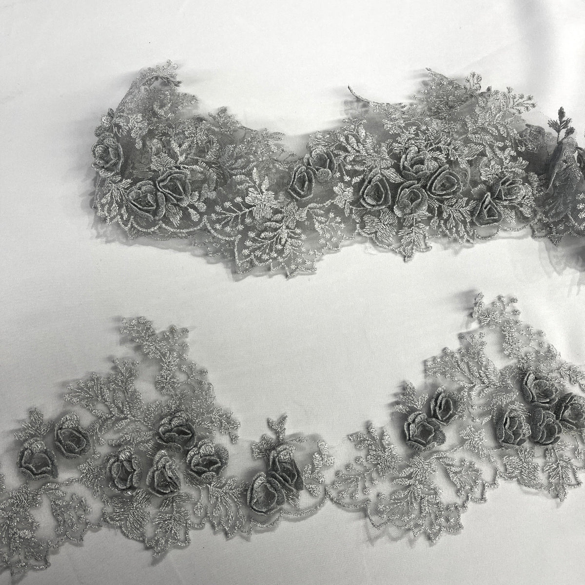Silver lace trim with 3D rose motifs embroidered with metalic thread on 100% polyester net mesh, featuring one flat unrolled length and one gathered bundle on a white background. LaceUSA #21853W