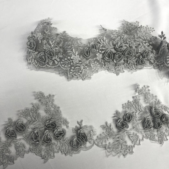Silver lace trim with 3D rose motifs embroidered with metalic thread on 100% polyester net mesh, featuring one flat unrolled length and one gathered bundle on a white background. LaceUSA #21853W