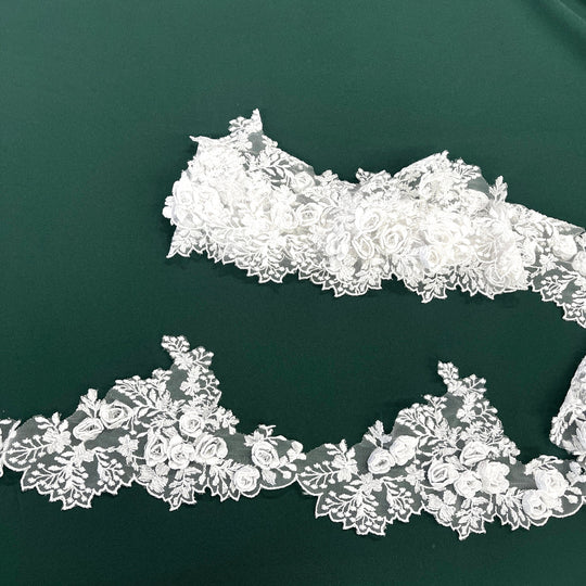 White lace trim with 3D rose motifs embroidered on 100% polyester net mesh,, featuring one flat unrolled length and one gathered bundle on a green background. LaceUSA #21853W
