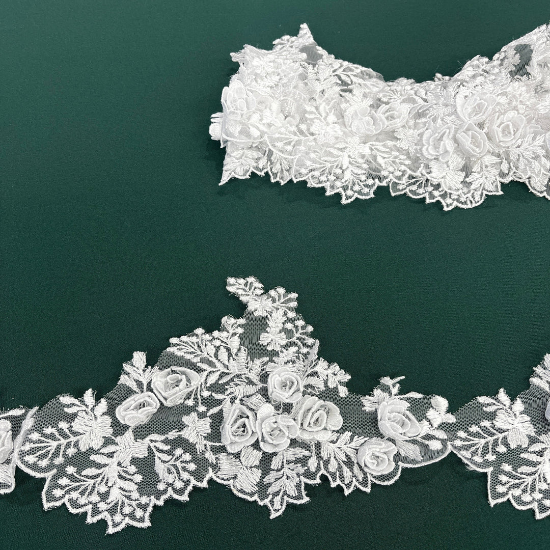 White lace trim with 3D rose motifs embroidered on 100% polyester net mesh, featuring one flat unrolled length and one gathered bundle on a green background. LaceUSA #21853W