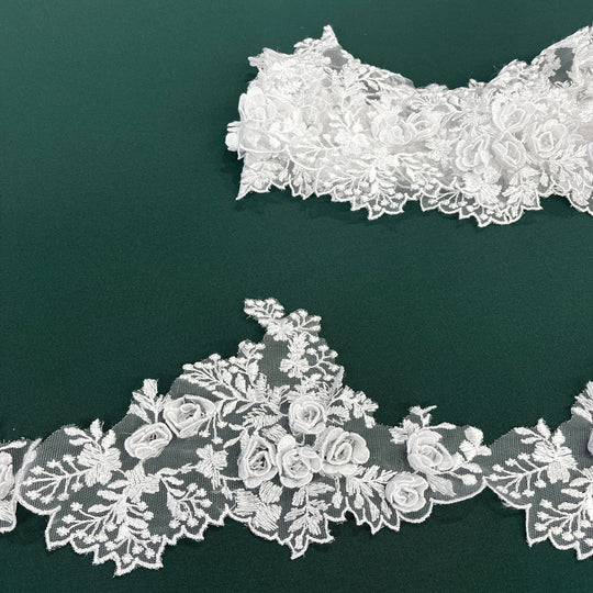 White lace trim with 3D rose motifs embroidered on 100% polyester net mesh, featuring one flat unrolled length and one gathered bundle on a green background. LaceUSA #21853W