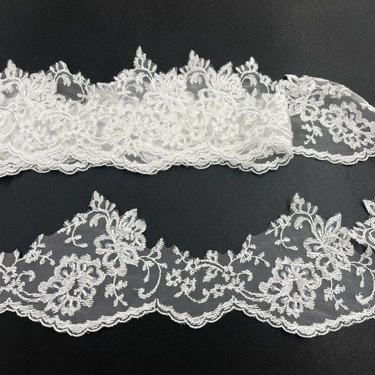 White beaded floral lace trim with scalloped edges, displayed in two horizontal strips featuring one flat unrolled length and one gathered bundle on a black background. Lace_USA #21356WBP
