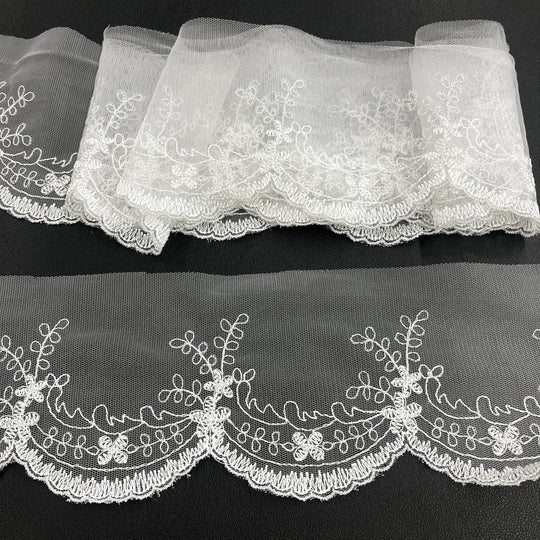 White floral lace trim with scalloped edges, embroidered on 100% polyester net mesh,, featuring one flat unrolled length and one gathered bundle on a black background. Lace USA 21734W