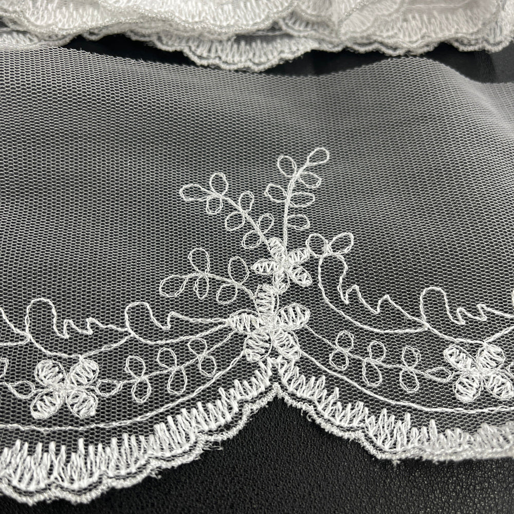Closeup of White floral lace trim with delicate embroidery and scalloped edges, shown in close-up against a dark background. Lace USA #21734W