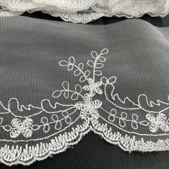 Closeup of White floral lace trim with delicate embroidery and scalloped edges, shown in close-up against a dark background. Lace USA #21734W