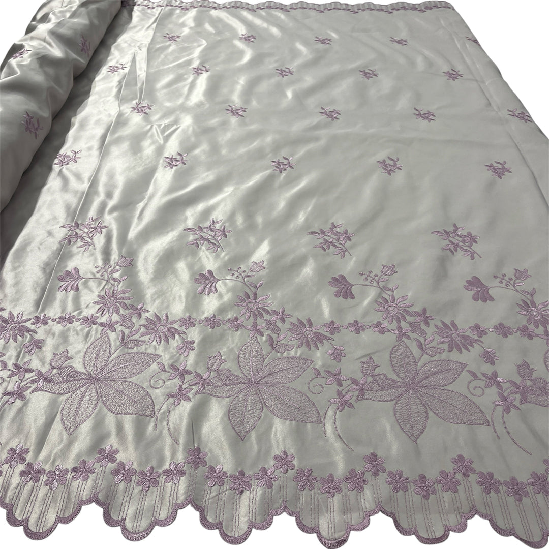 Yam satin fabric with embroidered floral patterns and a scalloped border, shown partially rolled on the left side.
