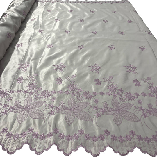 Yam satin fabric with embroidered floral patterns and a scalloped border, shown partially rolled on the left side.