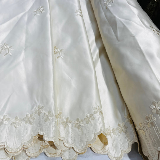 champagne satin fabric with delicate floral embroidery and a scalloped hem, draped to show its texture and pattern.